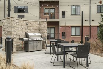 Outdoor table and chairs near a stainless steel grill enclosed by stone