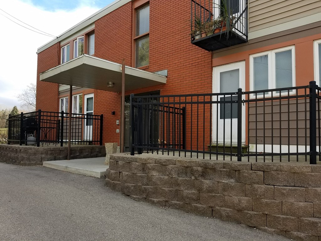 the front of a house with a stone retaining wall and a black fence