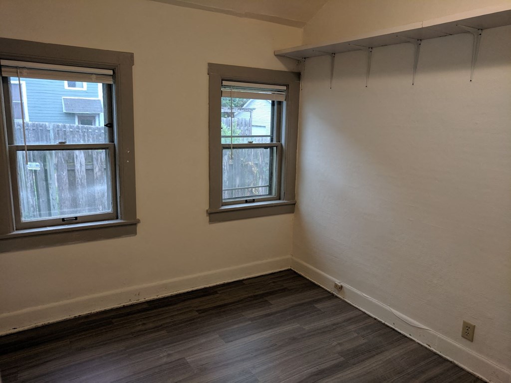 an empty room with two windows and a wooden floor