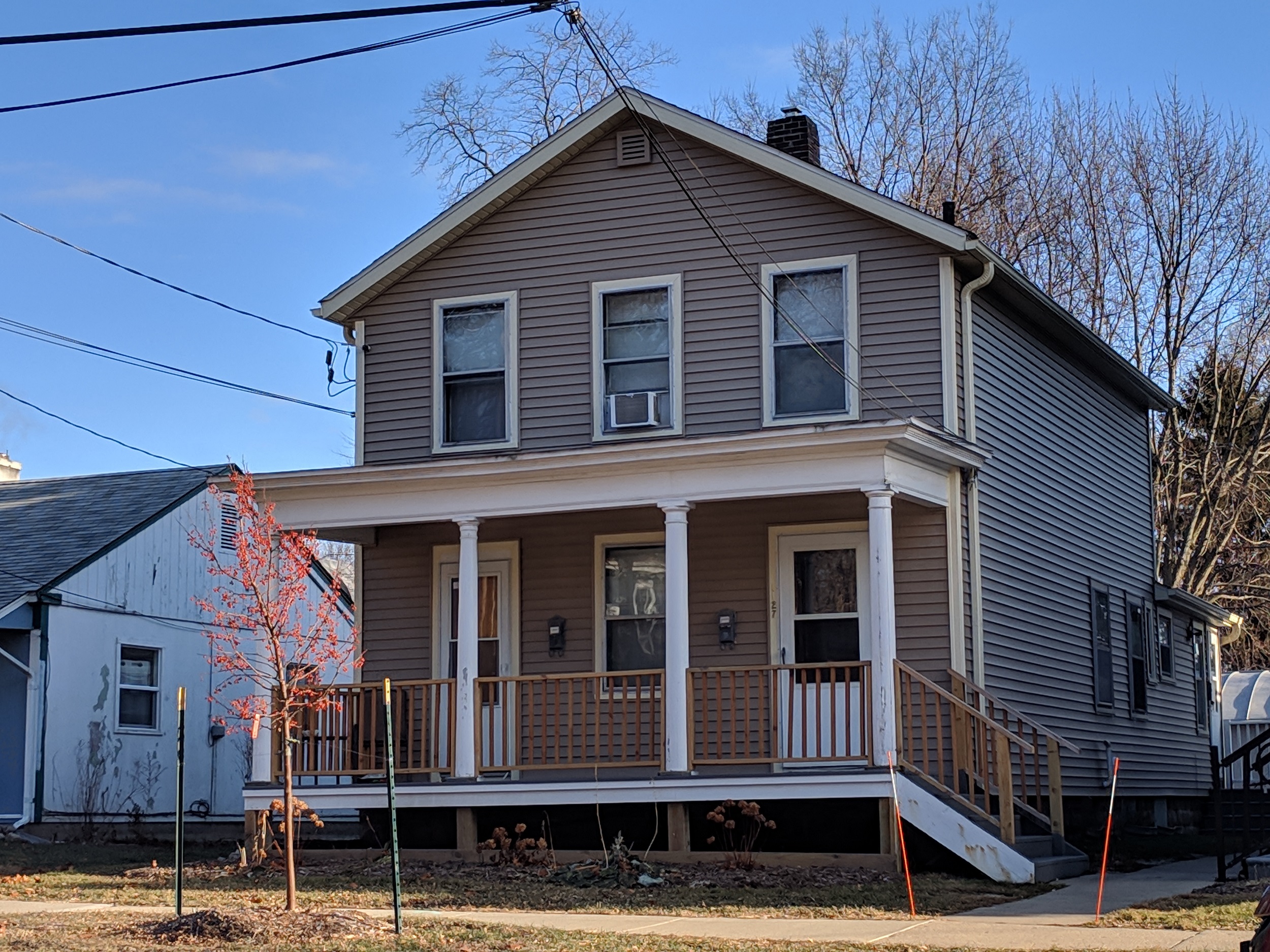 a gray house with a porch and a white house next to it