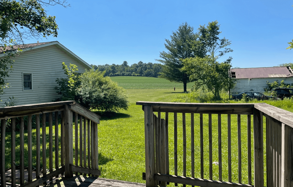 the view from the deck of a cabin with a field in the background