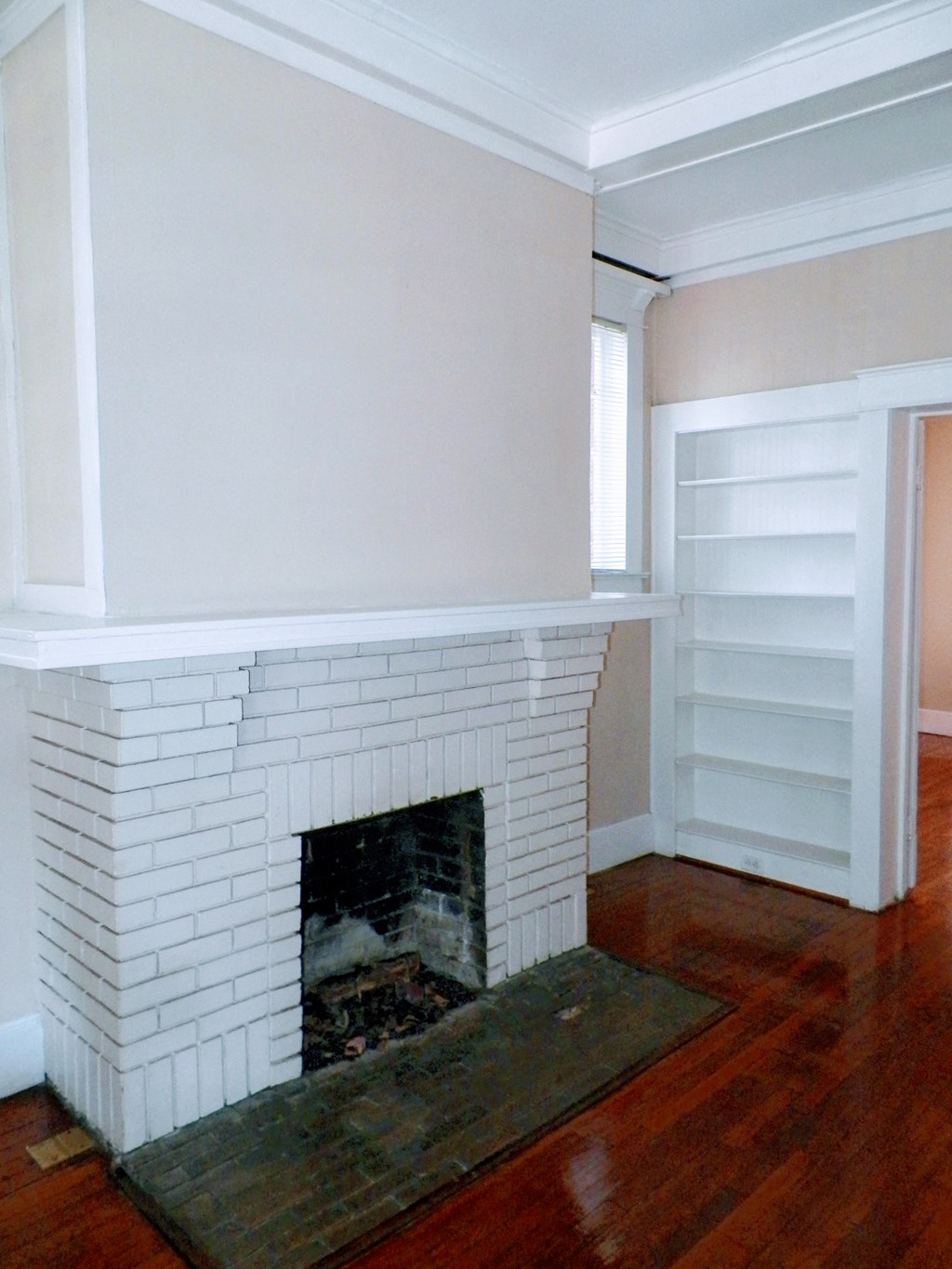 a white brick fireplace in a living room with a wooden floor
