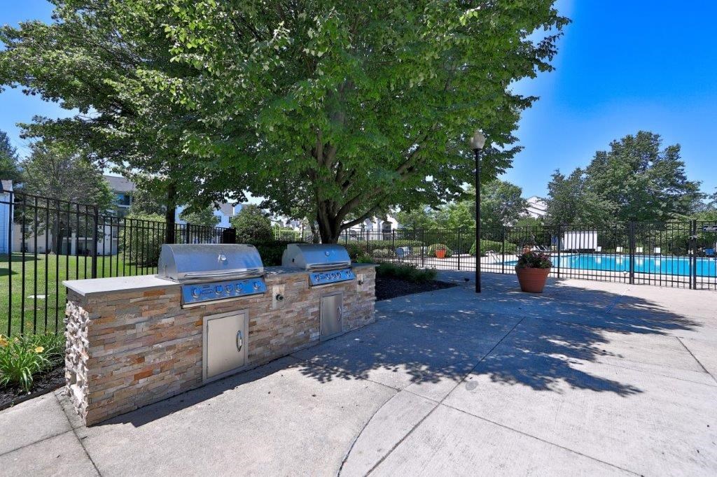 a barbecue grill with trees and a pool in the background