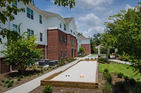 Outdoor shuffleboard court with shaded pavilion seating, landscaped surroundings, and a relaxing space for recreation and socializing.