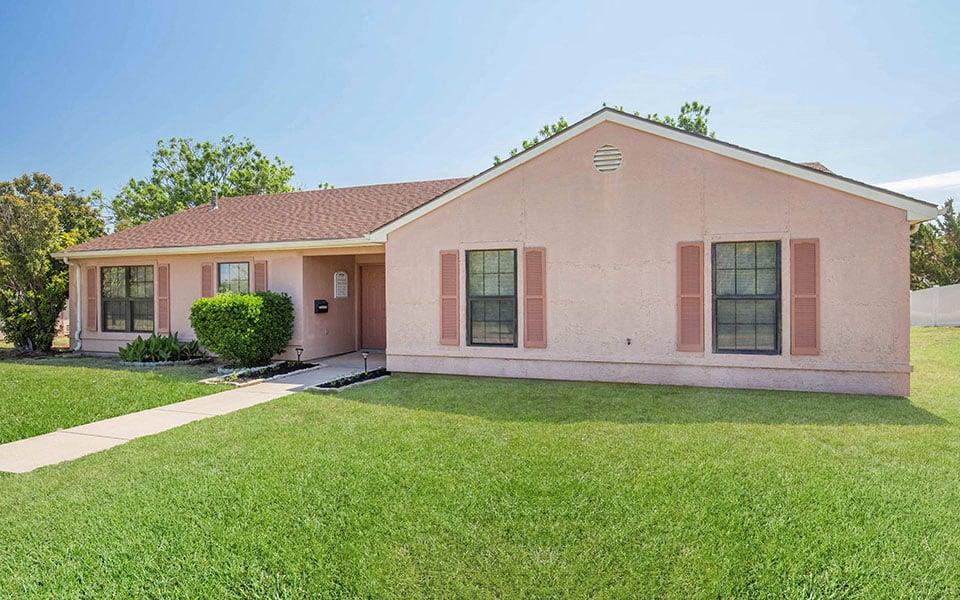 a pink house with a grass yard and a sidewalk