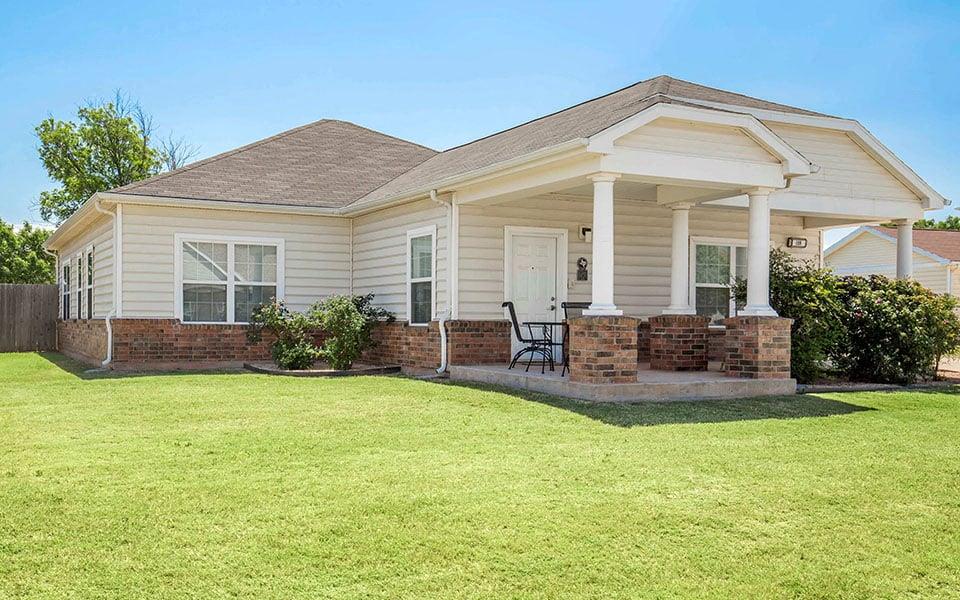 a small white house with a brick porch and a lawn