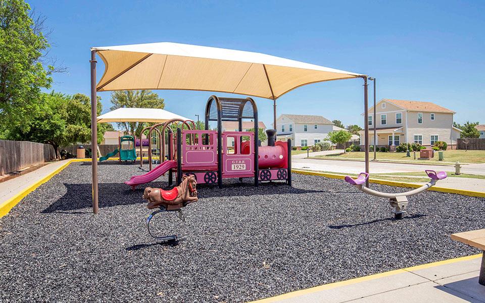 a playground with a pink swing set and two rocking horses