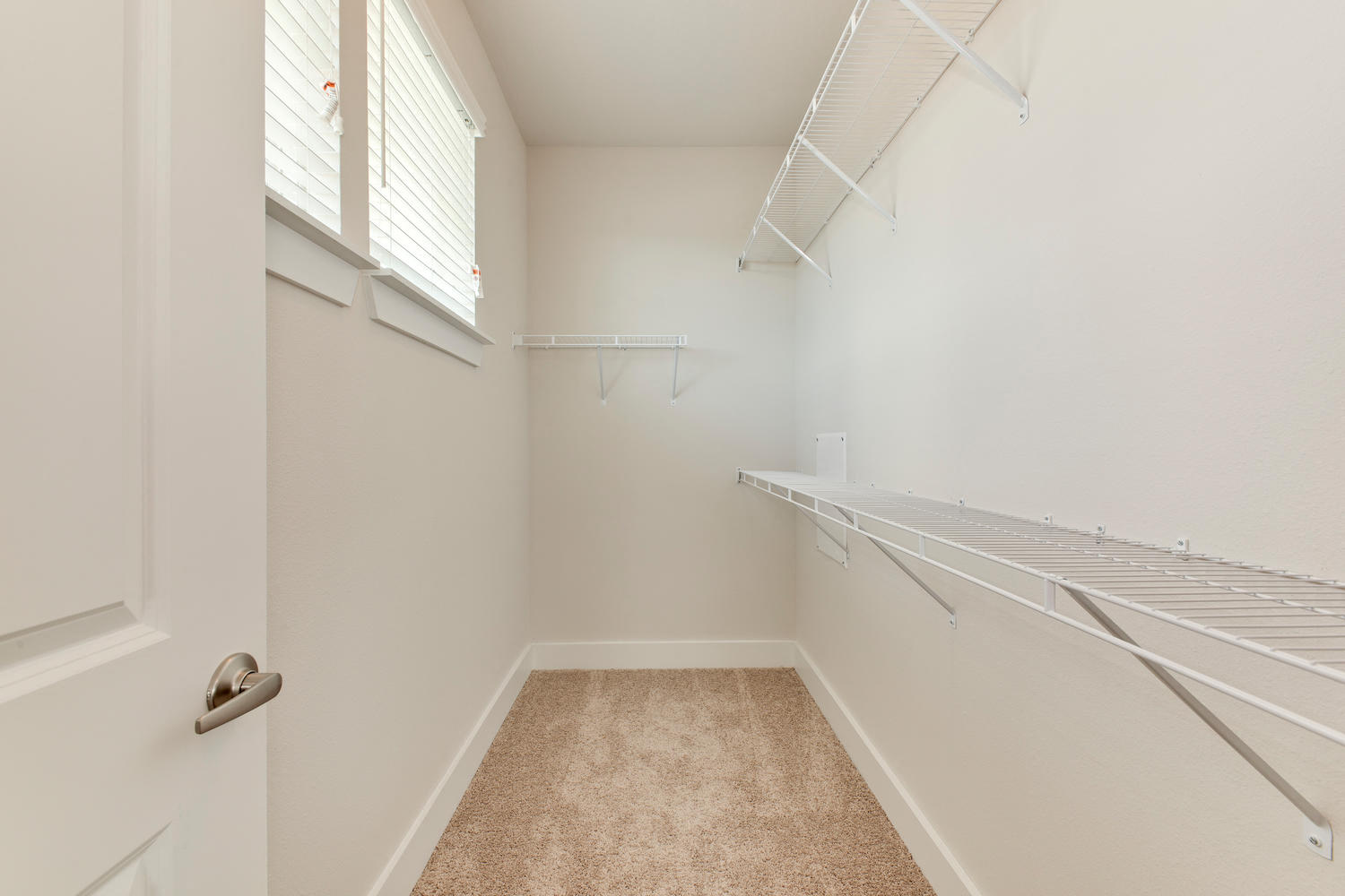 a spacious closet with white walls and shelves and a window