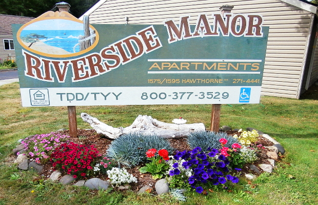 a sign for riverside manor apartments in front of a flower garden