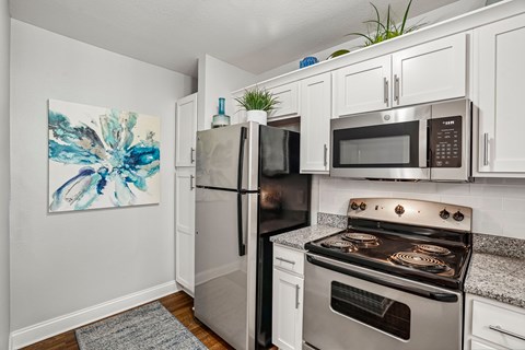A kitchen with a stainless steel refrigerator and oven, a microwave above the stove, and a painting on the wall.