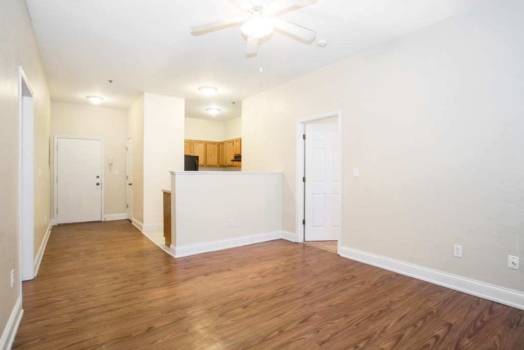 the living room and kitchen of an apartment with wood flooring and a ceiling fan
