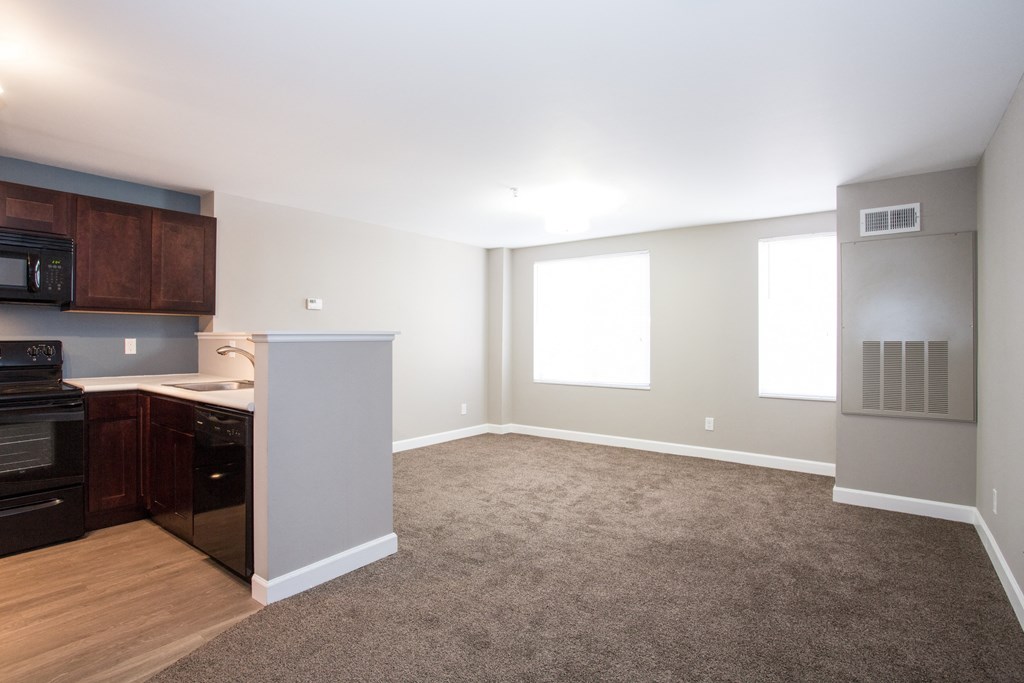 an empty living room with a kitchen with an oven and a sink