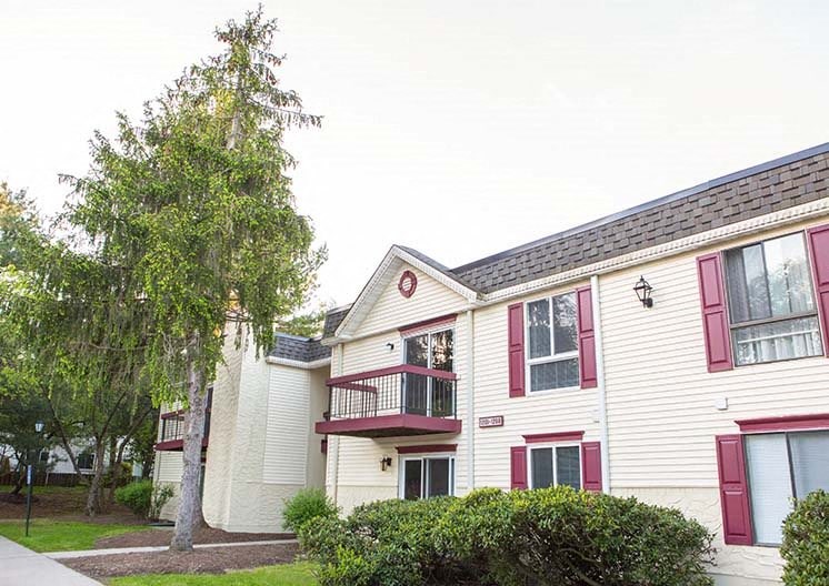 a white house with a red balcony and a tree