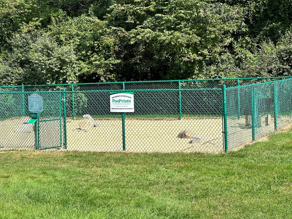 A green fence surrounds a sandy area with a sign that says PoopPrints.
