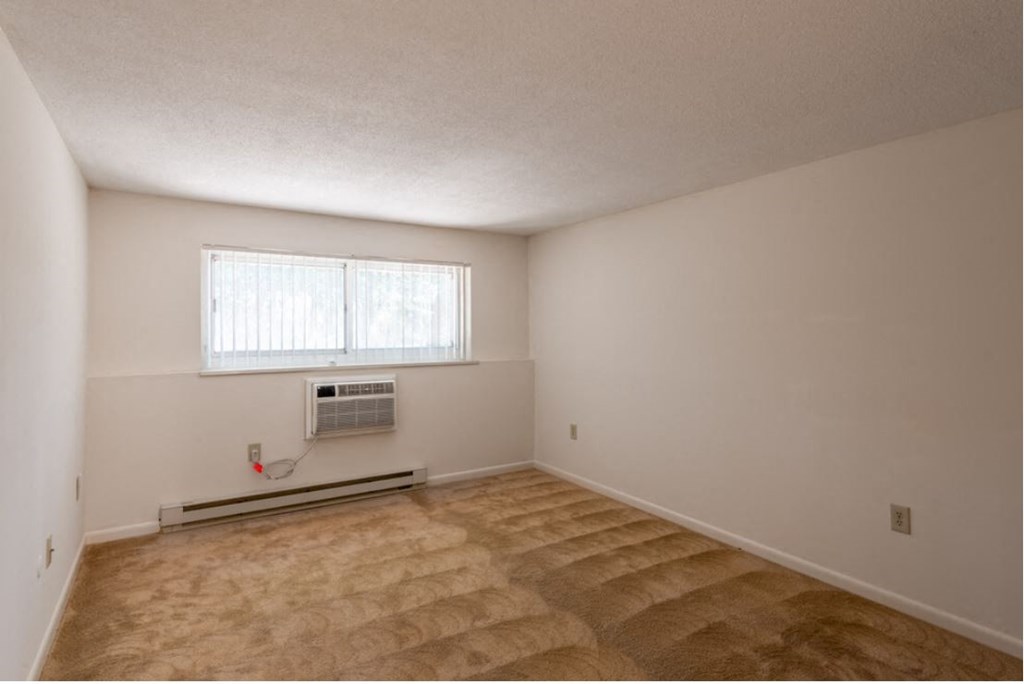 an empty living room with a heater and a window
