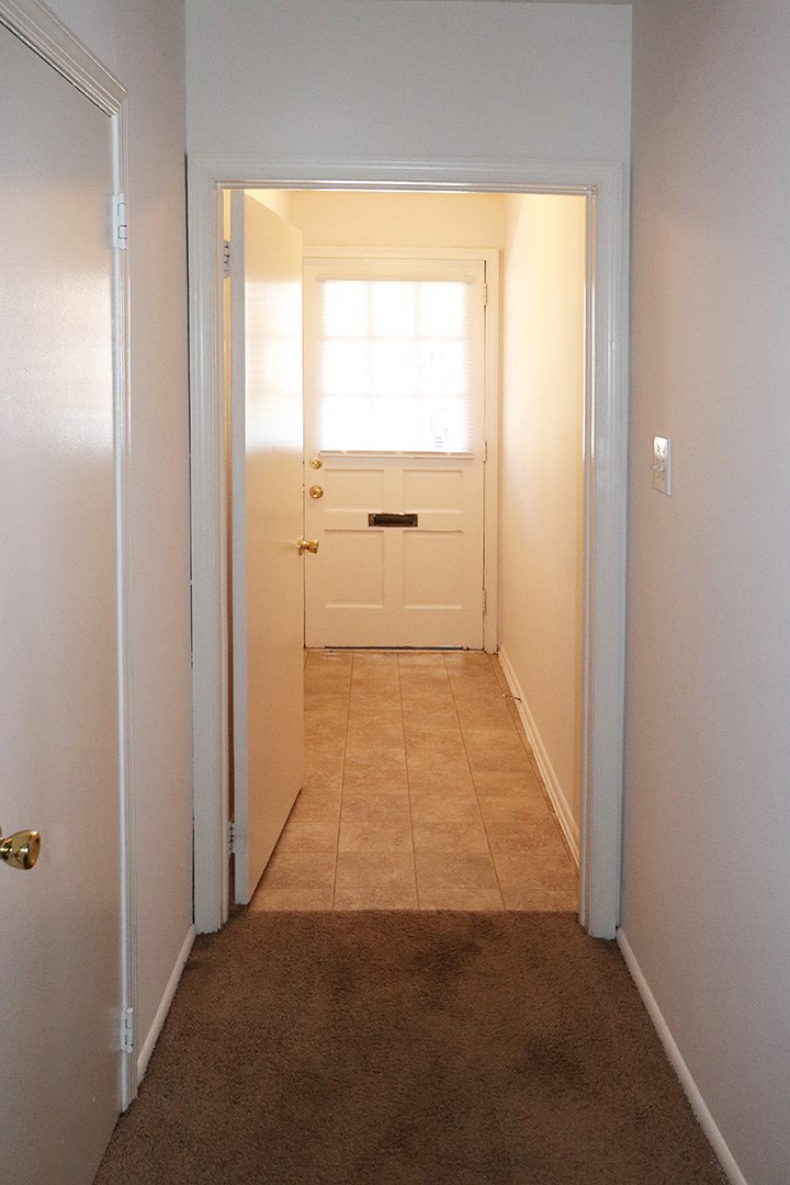 the hallway of a home with a white door and tiled floor