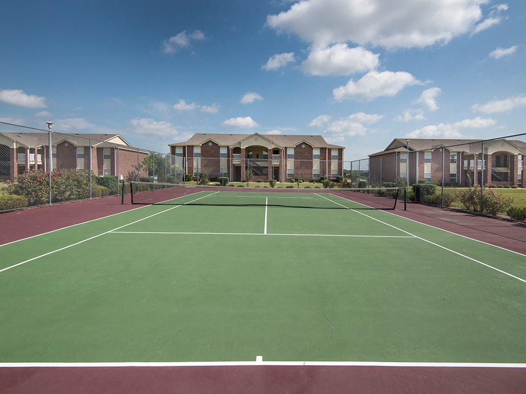 a tennis court with buildings in the background on a sunny day