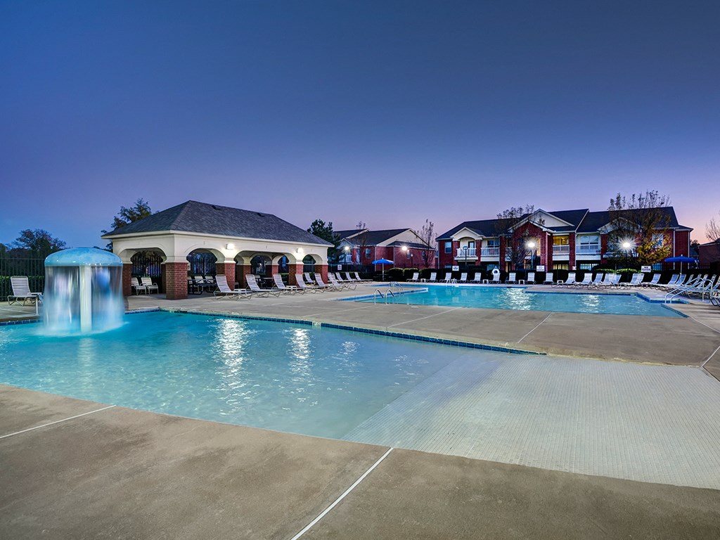 a swimming pool at night with apartments in the background
