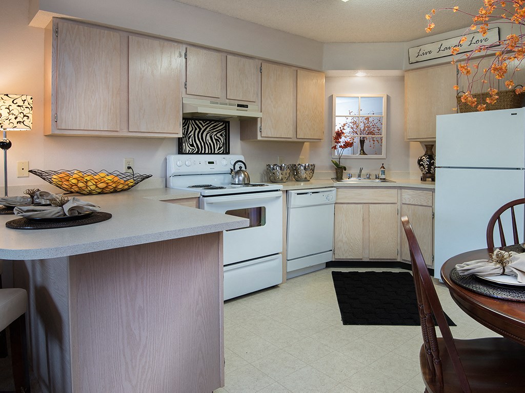 a kitchen with white appliances and a table with a bowl of fruit