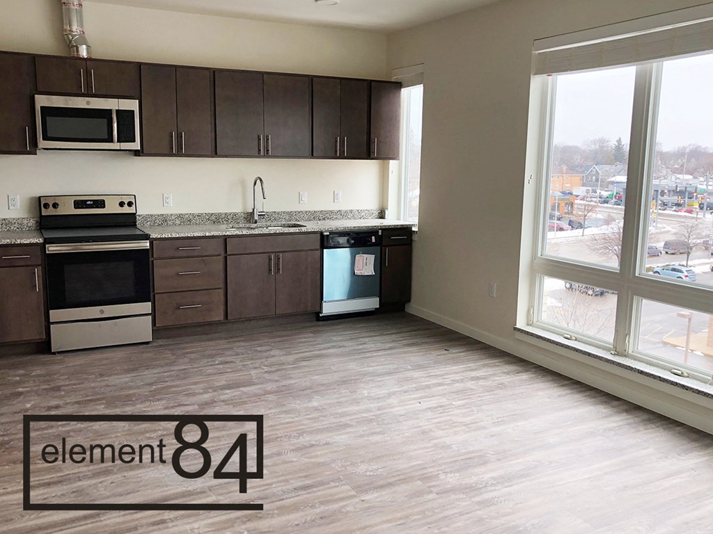 an empty kitchen with a large window and wood flooring