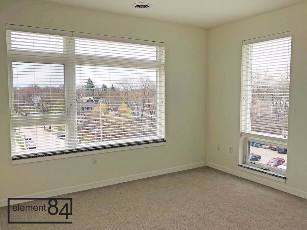 a living room with two large windows and a carpeted floor