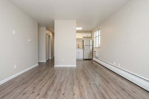 A spacious room with wooden flooring and a kitchen area in the background.