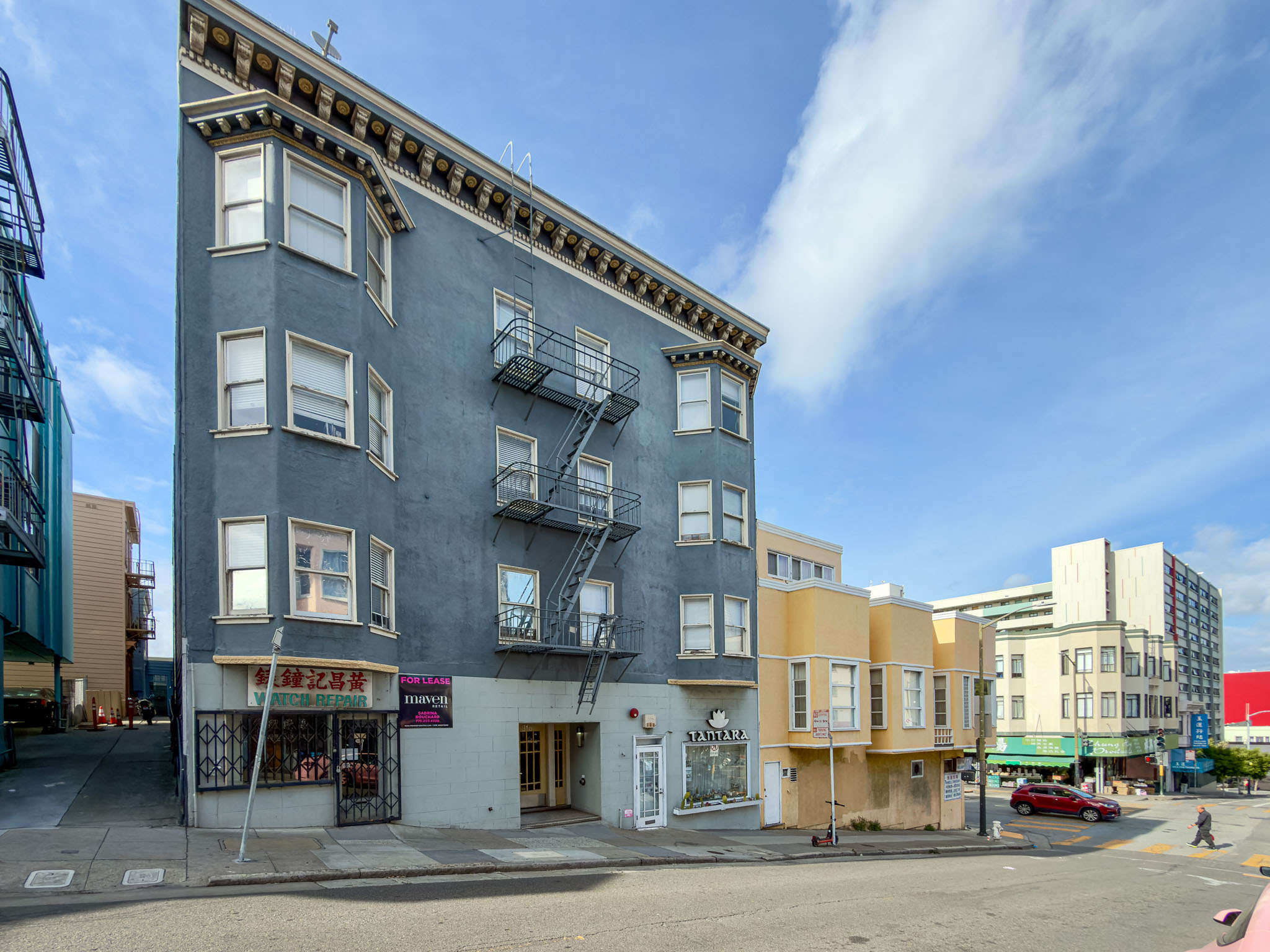 A street view of a multi-story building with a fire escape on the side.