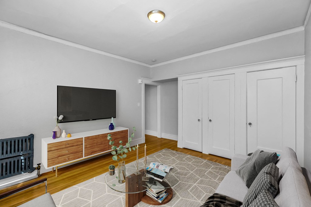 A living room with a grey couch, a wooden cabinet, a flat screen TV and a radiator.