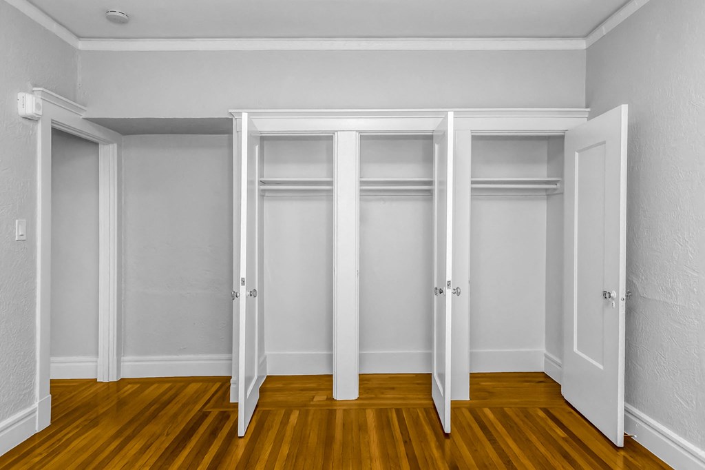 A room with white walls and wooden floors with three white doors.