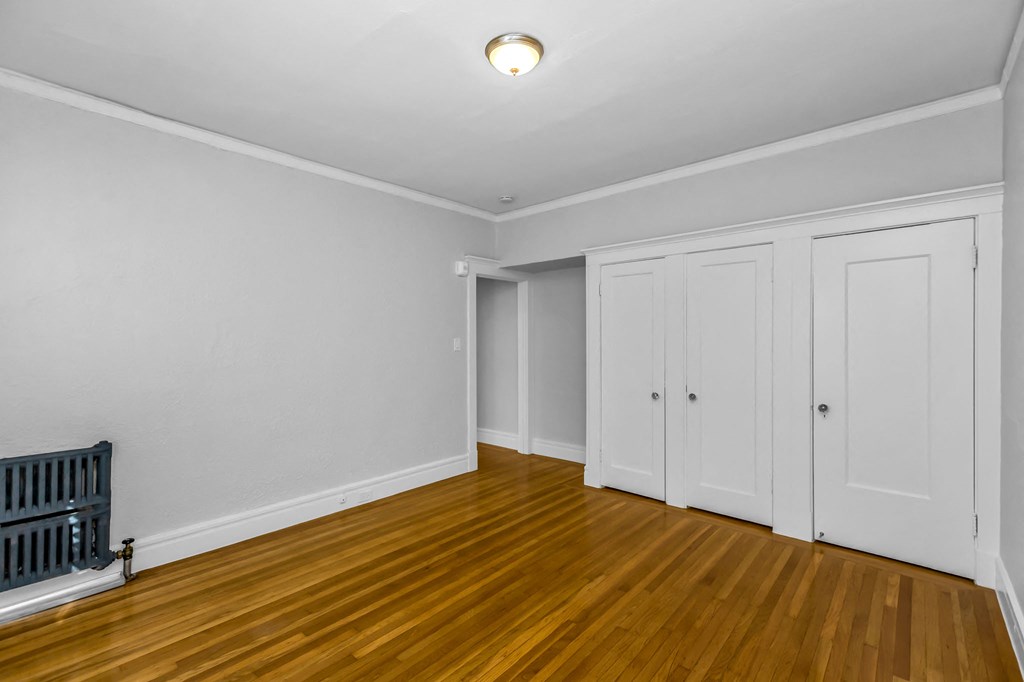 A room with wooden floors and white walls with a radiator on the left side.
