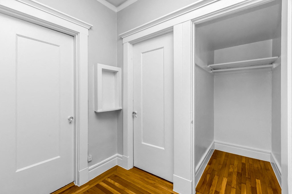 A white closet with a shelf and a door with a towel hanging on it.