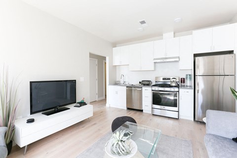 a living room with a tv and a kitchen with stainless steel appliances