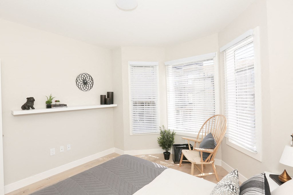 a bedroom with a bed and a chair and three windows