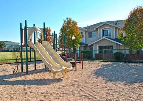 a playground with a slide and a picnic table in front of a house