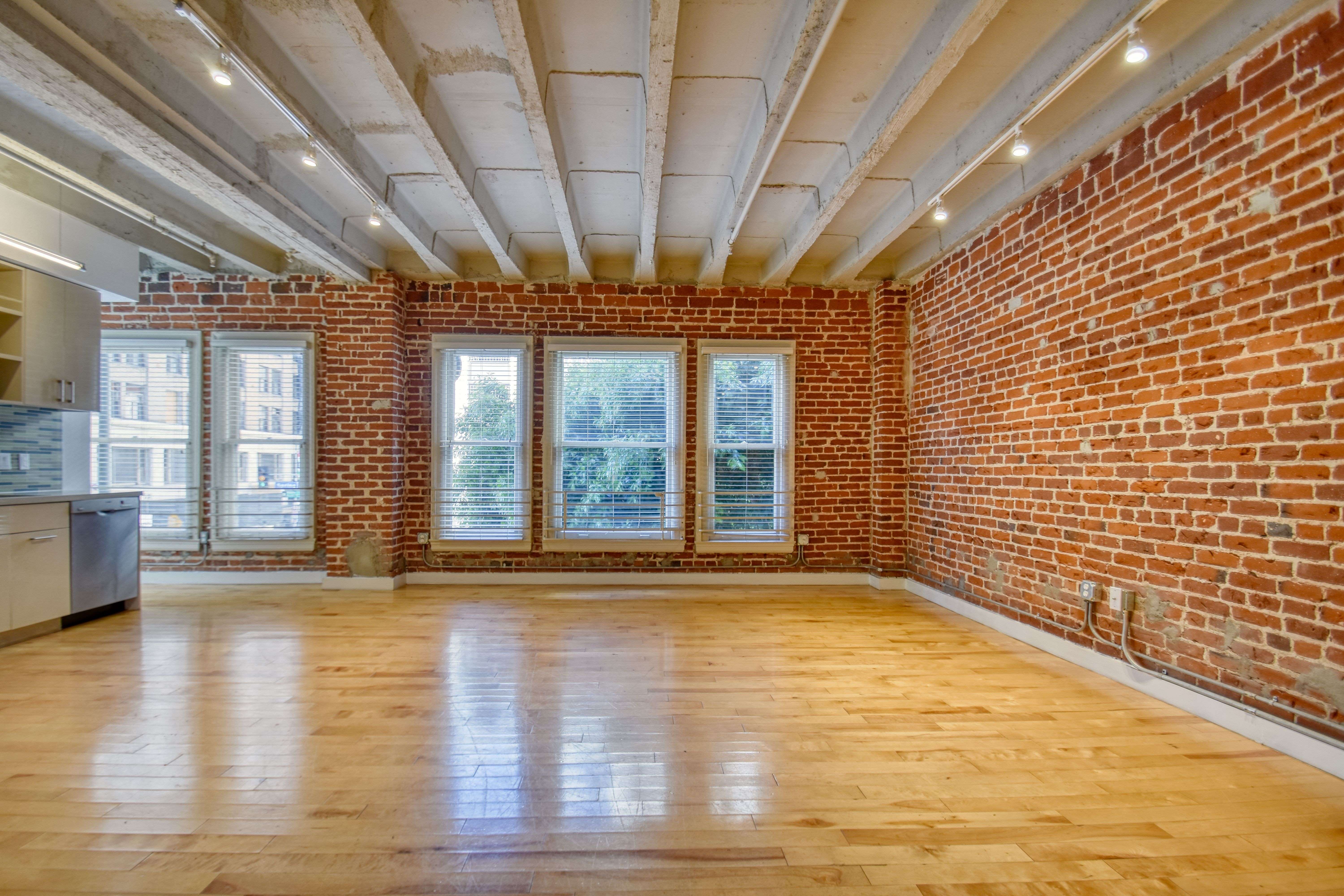 A large empty room with wooden floors and a brick wall.