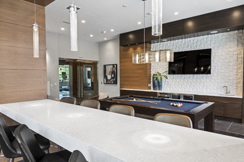 A pool table is in the middle of a room with a bar and a TV.