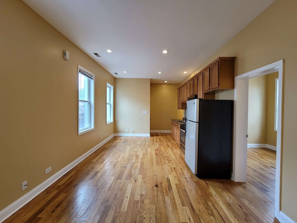 an empty living room with a kitchen and a refrigerator