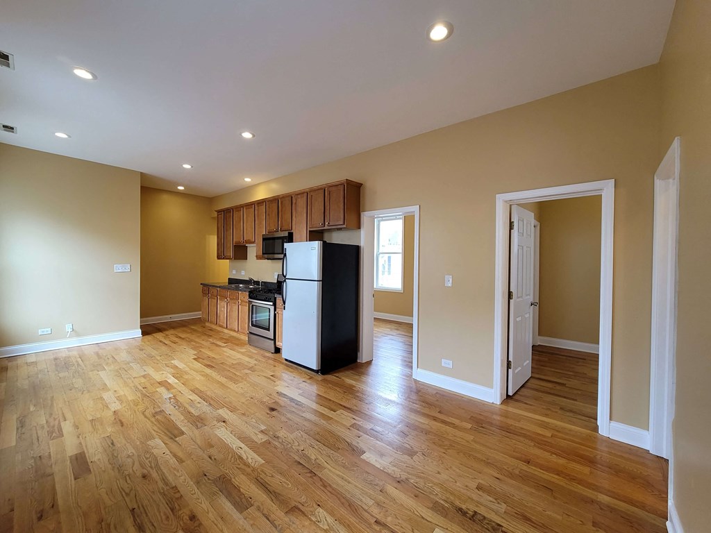 an empty living room with a kitchen and a refrigerator