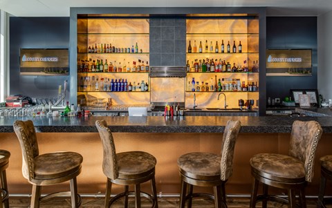 a bar with four stools in front of a bar filled with bottles