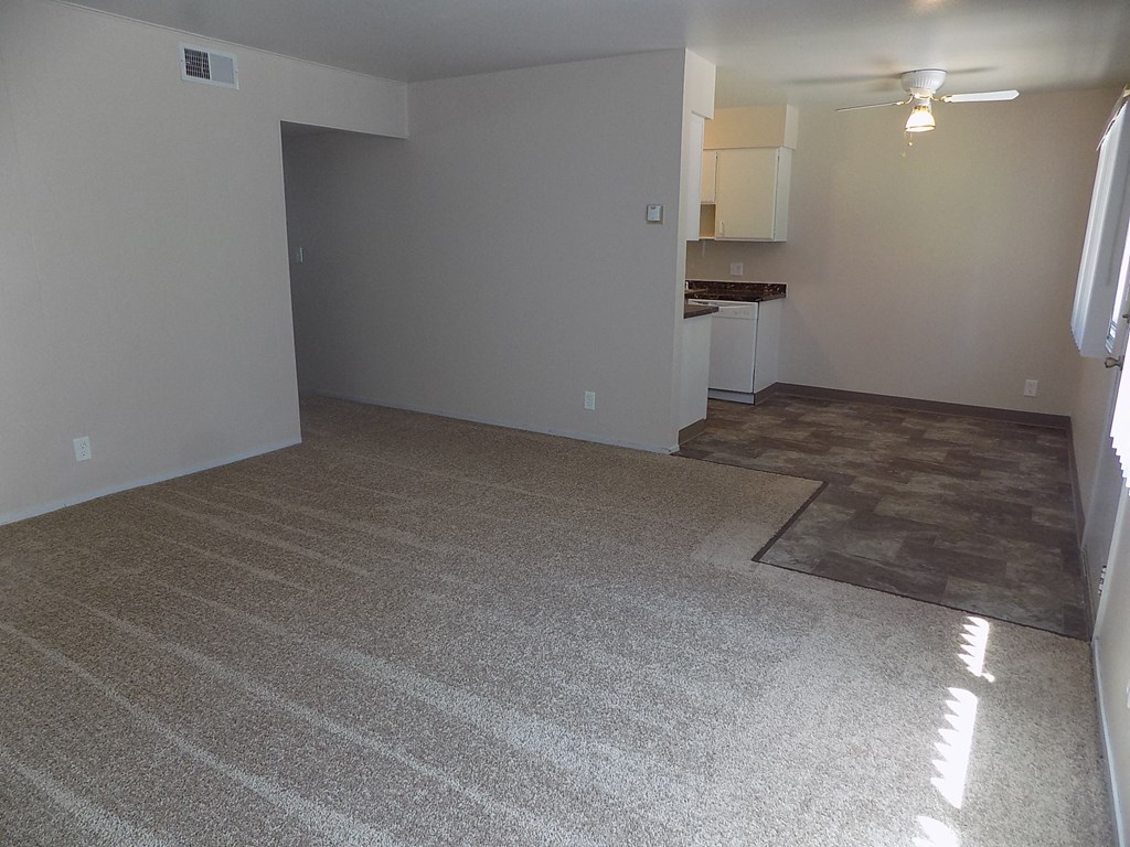 an empty living room with carpet and a kitchen