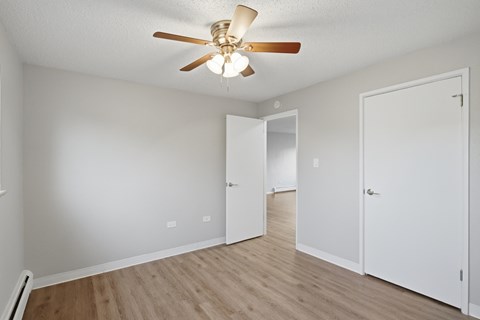 A room with a ceiling fan and light fixture, two doors, and a wooden floor.