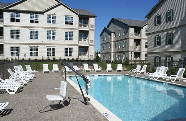 a swimming pool with white chairs in front of an apartment building