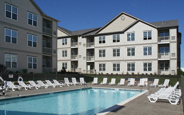 a swimming pool with white chairs in front of an apartment building