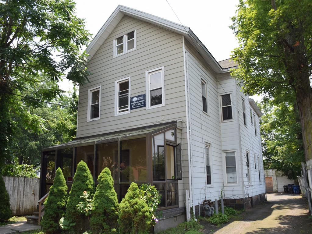 A house with a grey facade surrounded by green trees.