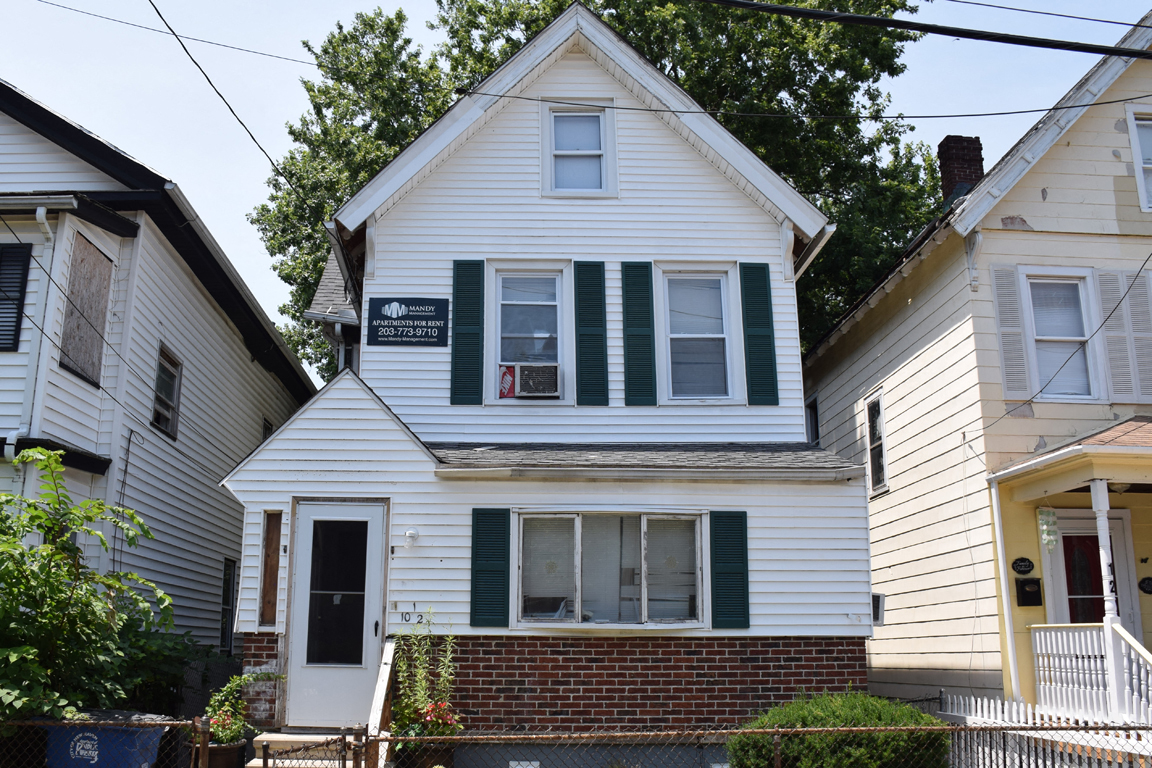 A white house with green shutters and a sign that says "For Sale".