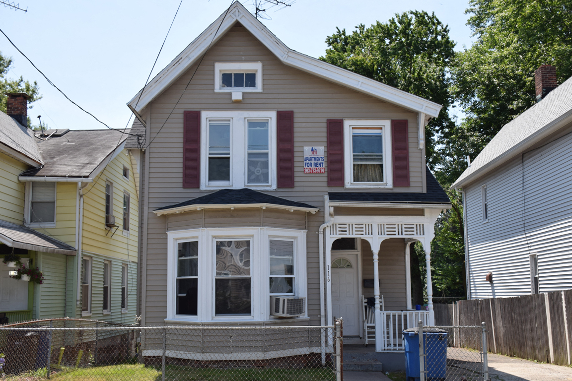 A two-story house with a front porch and a sign on the front window.