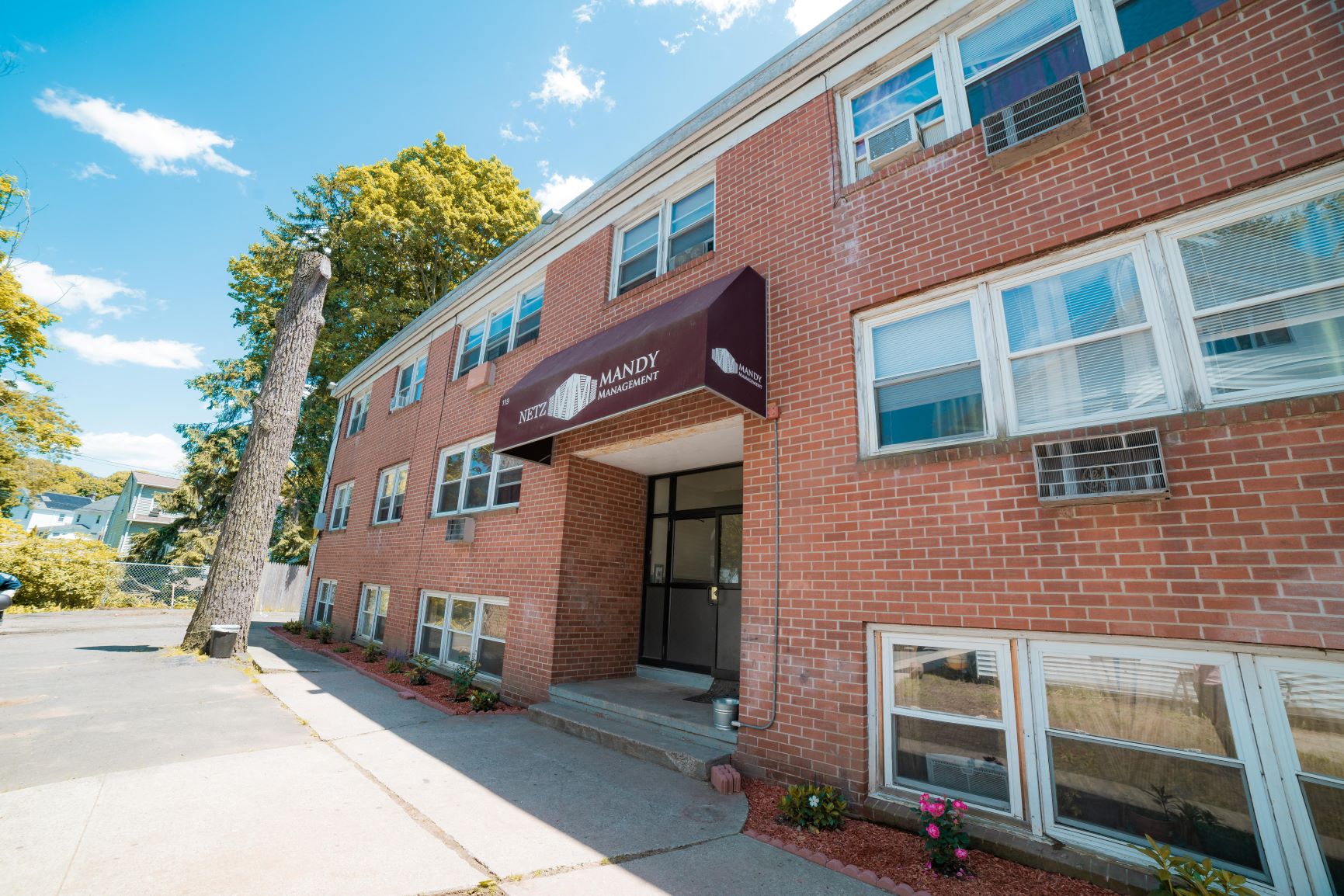 The image shows a red brick building with a brown awning and white windows.
