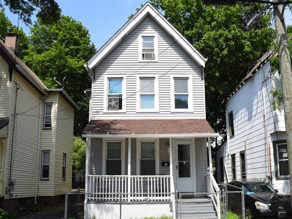 A two-story house with a white porch and a black car parked in front.