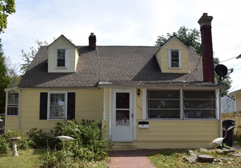 A small yellow house with a white door and a chimney.