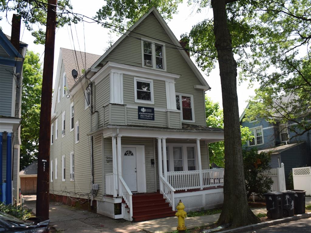 A two-story house with a white porch and a yellow fire hydrant in front.
